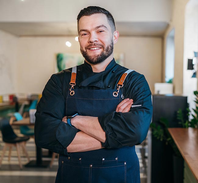 Male with a beard and arms folded smiles at the camera