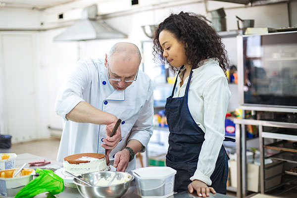 Chef teaching young female student how to ice a cake